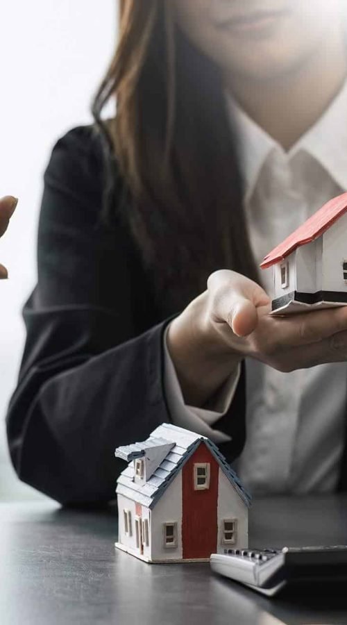 Conseiller protégeant symboliquement un modèle de maison à Caen pour diagnostic immobilier.